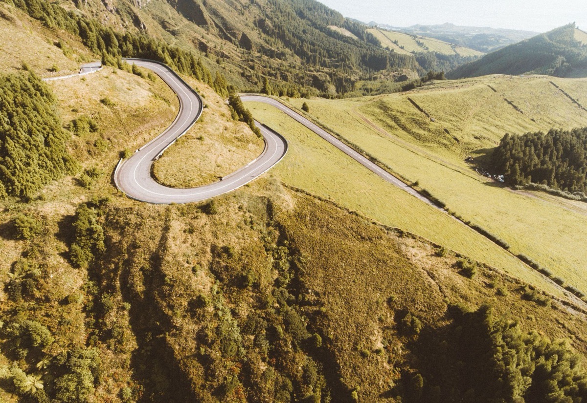 A winding road climbing through green mountains toward the sea